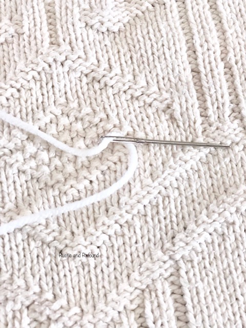 Using yarn and a large needle to stitch the outside of the sweater circle.