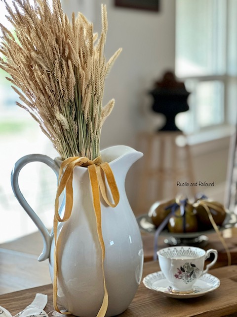 White pitcher holding golden grass tied with gold ribbon
