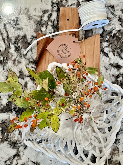 Foraged red berries - foliage in a white basket on a breadboard.