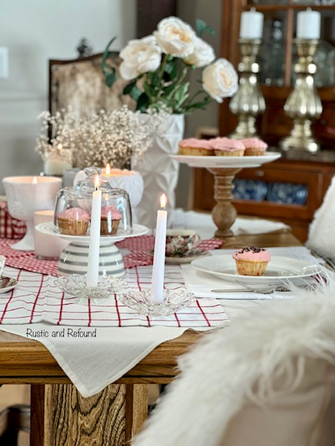 An end view of a simple and sweet Valentine' Day table for two with candles and pink cupcakes.